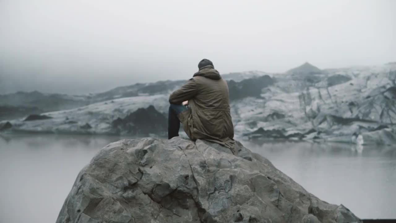 后视图的年轻游客坐在岩石上，看着冰川泻湖。独自探索冰岛的人视频素材