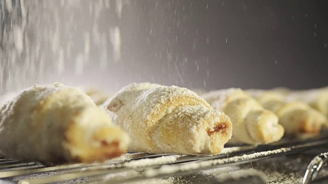 面包师把糖霜撒在美味的饼干上。新鲜牛角面包，上面撒糖粉。慢动作视频素材