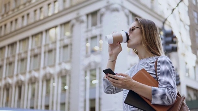年轻忙碌的女商人戴着太阳镜拿着文件，用着智能手机，在街上喝着咖啡视频素材