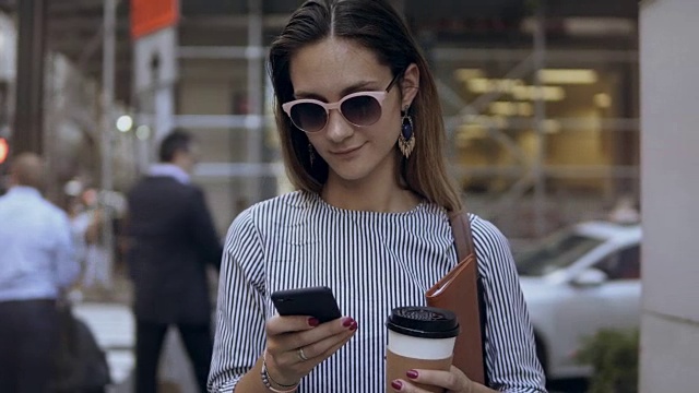 年轻美丽的女商人拿着咖啡杯和文件在拥挤的街道上使用智能手机的肖像视频素材