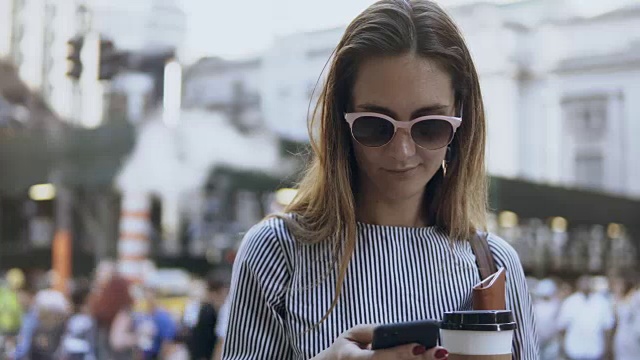 年轻美丽的女商人站在拥挤的街道上拿着咖啡和文件，用智能手机视频素材