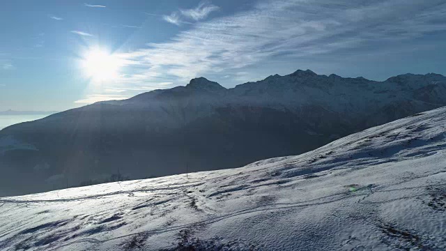 在阳光明媚的日子里，向前鸟瞰冬季雪山与滑雪轨道。背光白色阿尔卑斯山脉雪季节建立与阳光照耀。4k无人机飞行建立镜头视频素材