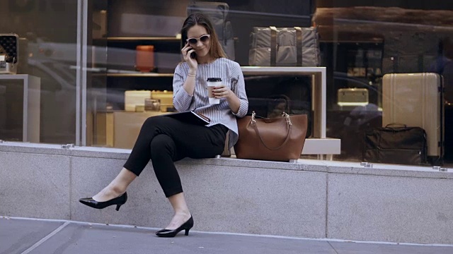 年轻时尚女商人的咖啡休息时间。快乐的女性坐在橱窗附近，用智能手机聊天视频素材