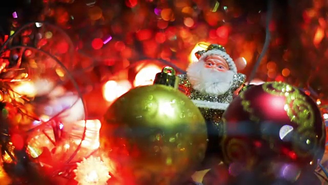 微型圣诞老人的形象之间的两个玩具悬挂的小装饰品的圣诞树。木制表面上的银色圣诞老人被闪烁的灯光包围着视频下载