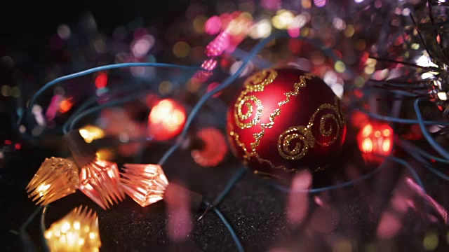 圣诞节和新年装饰。把小玩意挂起来。抽象模糊散景假日背景。一个红色的圣诞树玩具球放在木制的表面上，周围环绕着花环。视频素材