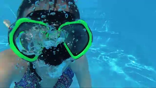 戴着面具的女孩在游泳池里看着镜头，冒着泡泡视频下载