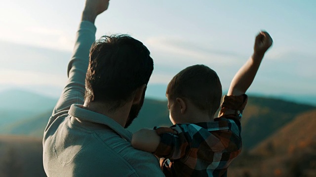 父亲抱着儿子，他们在山顶上举起双手视频素材
