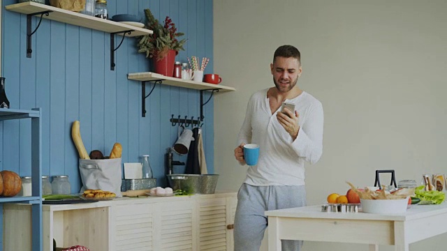 快乐的男人在厨房唱歌跳舞，早上在家里用他的智能手机视频素材