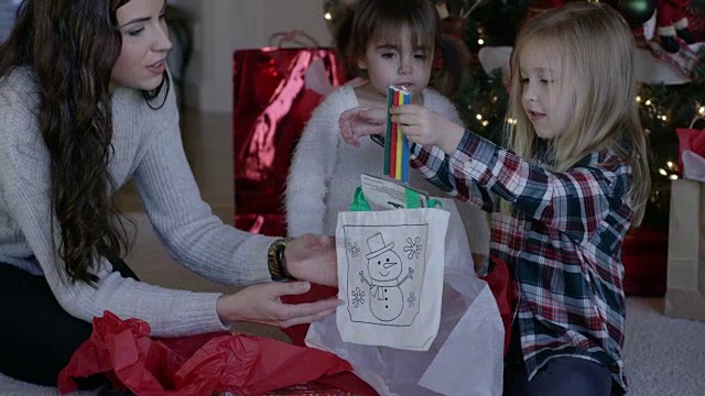 两个小女孩在圣诞树前和妈妈一起打开圣诞礼物视频素材