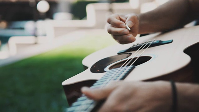 在阳光明媚的夏日里，年轻的音乐家在公园里换弦，重新弹吉他。英俊的创造性的人视频素材