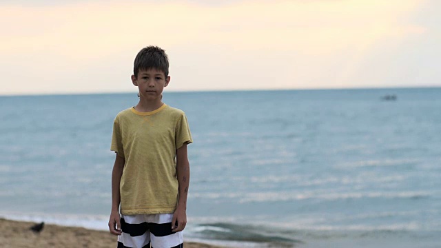 男孩站在海边的沙滩上看着镜头视频下载