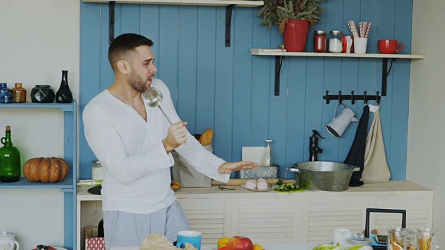有吸引力的年轻有趣的男子跳舞和唱歌在厨房做饭在家里的慢动作视频素材