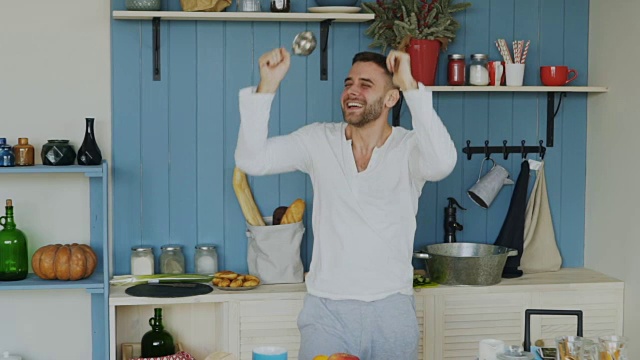 英俊的年轻有趣的男子跳舞和唱歌在厨房做饭在家里的慢动作视频素材