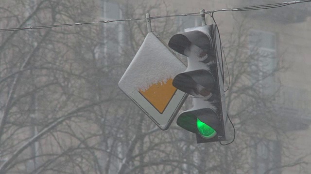 暴风雪期间，雪中的红绿灯控制交通。龙卷风来临时，大雪使道路上汽车的行驶变得复杂。特写镜头视频下载