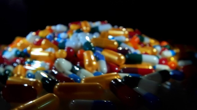 Сolorful胶囊的药物躺在桌子上的黑色背景视频下载