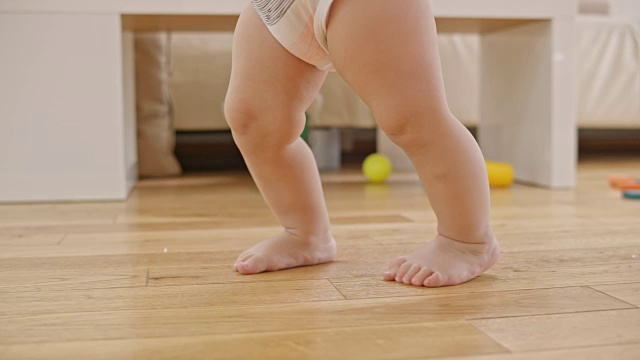 一个赤脚婴儿在木地板上行走的腿视频素材
