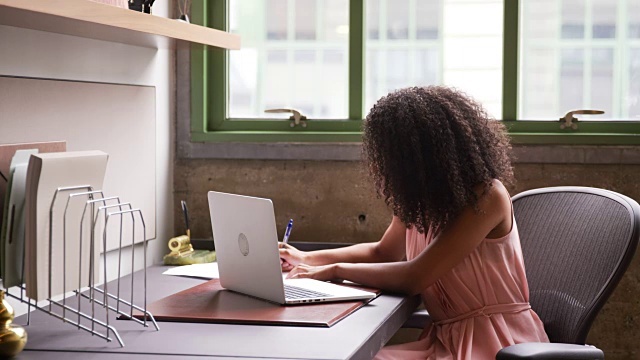 年轻的黑人女性在一个小办公室里用手提电脑独自工作视频下载
