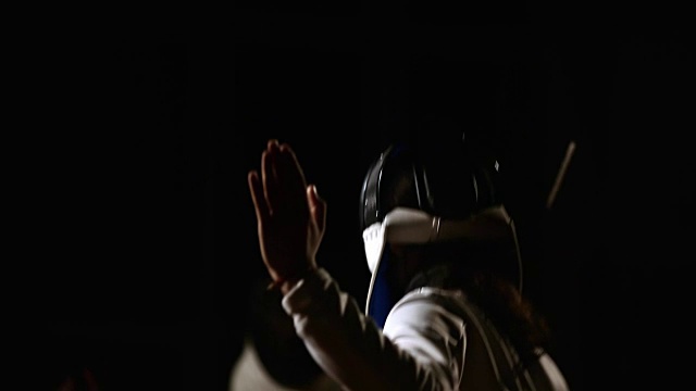一个男人的特写镜头戴着一个头盔的击剑格斗与一个对手在一个黑暗的背景与剑。围绕轴的移动和焦点从前景改变到背面视频素材