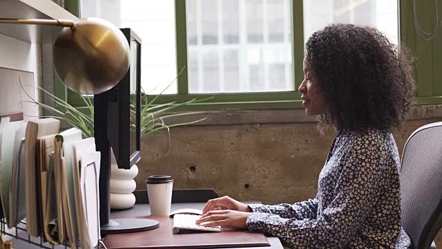 一个年轻的黑人妇女在办公室里使用电脑，侧面视频素材