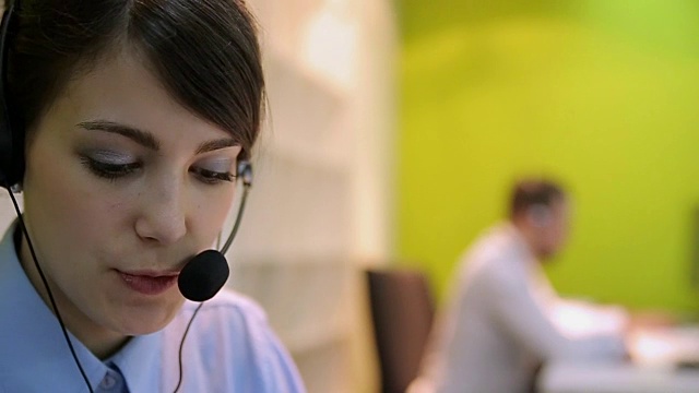 年轻的女商人戴着耳机在呼叫中心的团队陪同下工作。视频素材