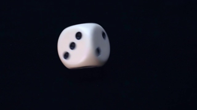 白色骰子旋转着落下，并以慢动作跳到黑色的表面视频素材