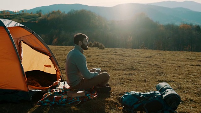 一个人坐在山上，喝着咖啡野营视频素材
