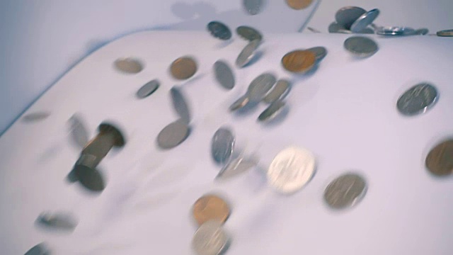 闪亮的金属硬币在倾斜的白色表面慢动作滚动视频素材