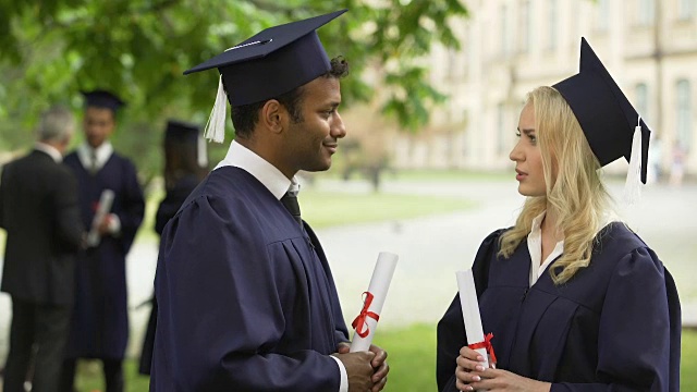 学生们穿着毕业礼服拿着毕业证书交谈、握手、拥抱视频素材