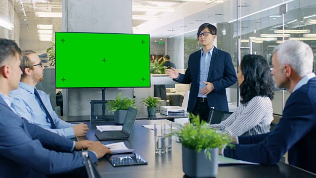 亚洲商人给他的商业同事的报告/报告，指向结果指向绿色色度键屏幕墙电视。视频素材