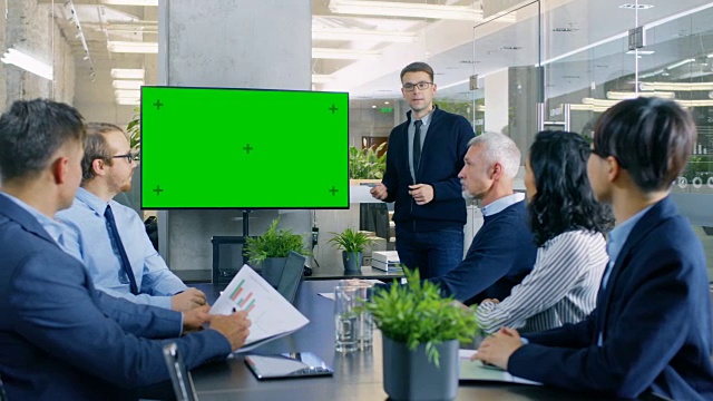 商人指着绿色度键屏幕墙电视向他的同事做报告/演示。视频素材