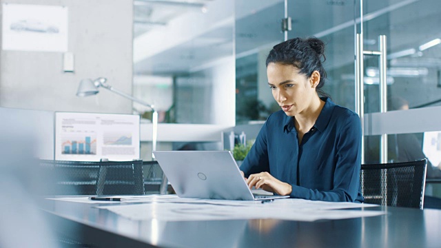 美丽的女性数据分析师坐在桌子上用笔记本电脑工作。现代办公环境中的时尚女性。视频素材