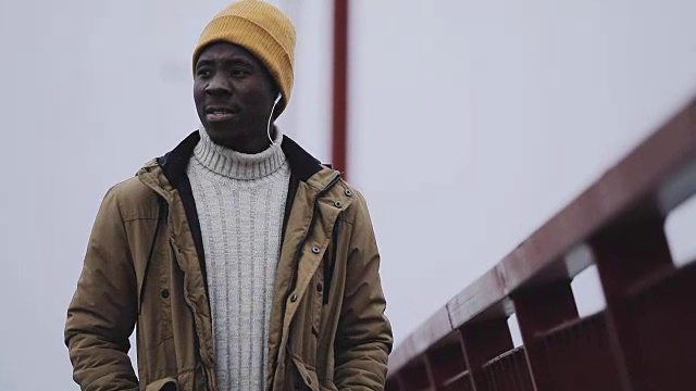 一个年轻的黑人在寒冷的冬天在桥上听音乐视频素材
