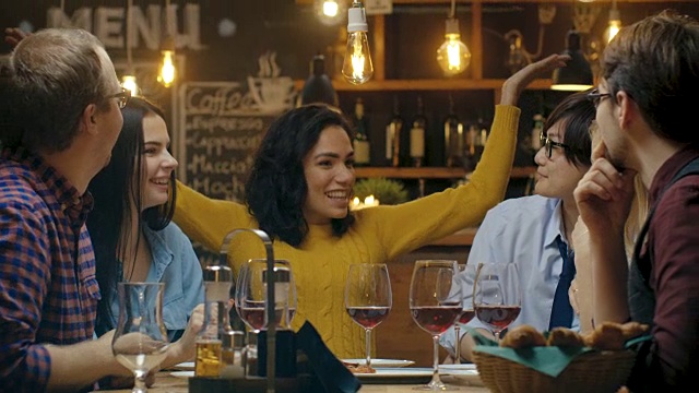 在酒吧/餐厅美丽的西班牙妇女与她亲爱的朋友分享好消息，他们热烈祝贺她和鼓掌。他们坐在时尚潮人的场所。视频素材