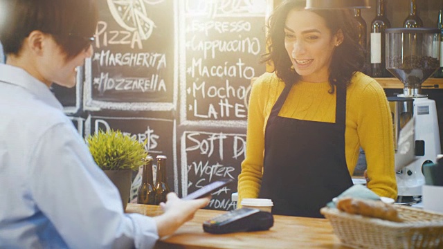 在咖啡馆里，一位西班牙美女正在为一位通过非接触式手机向信用卡系统付款的顾客制作外卖咖啡。视频素材