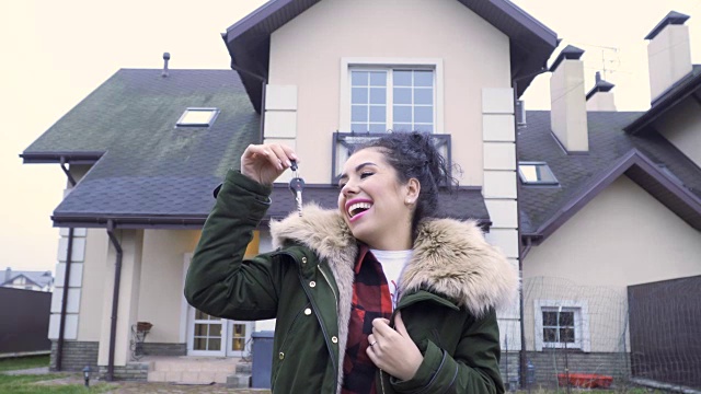快乐的漂亮女人拿着钥匙在她的新房子前视频素材