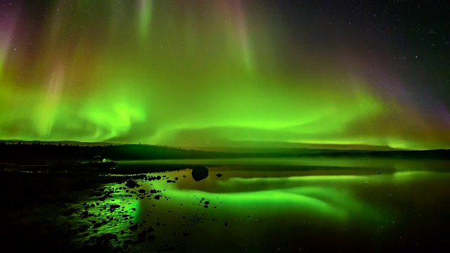 北极光滚过一个湖-一层明亮的滚动北极光反射在一个岩石湖的时间推移视频。视频素材