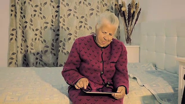 一个80岁老太太坐在床上的特写，看着她的照片在平板电脑上的慢动作。视频素材