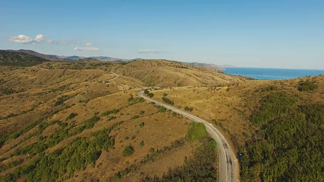 空中:高速公路穿过丘陵地带，有遥远的山脉和蓝色的海洋视频下载