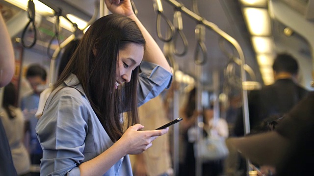 一名年轻女子在火车上抓着把手，使用智能手机视频素材