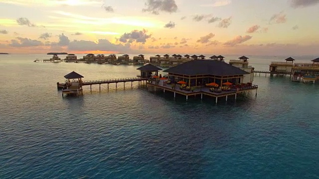 无人机在日落的一个风景优美的热带岛屿和度假酒店与水上平房在马尔代夫。视频素材