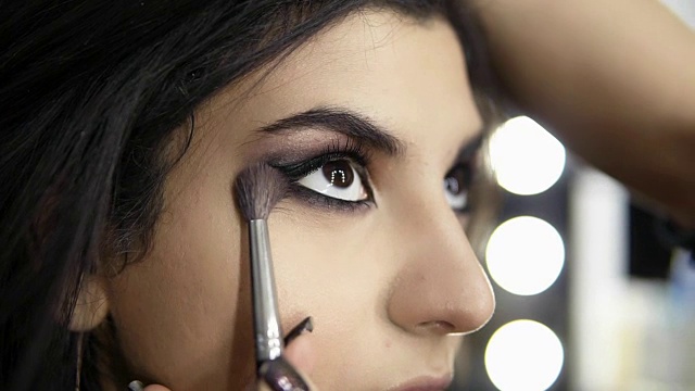 专业化妆师的手，用特殊的刷子将眼影刷到模特的眼睛上。美容、化妆和时尚概念。Slowmotion拍摄视频素材