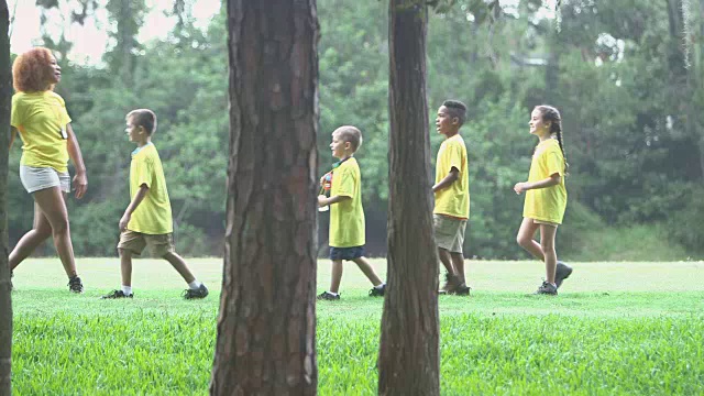 营地辅导员带着孩子们排成纵队在公园里散步视频素材