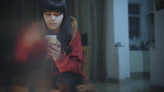年轻单身女子在晚上使用智能手机。视频下载