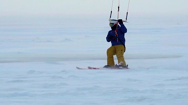 慢动作:一名男运动员正在滑雪板上放风筝。他在一个大湖的冰面上打滚。翻滚时，他会进行各种跳跃、动作和其他练习。雪板上的雪向不同的方向飞舞。视频素材
