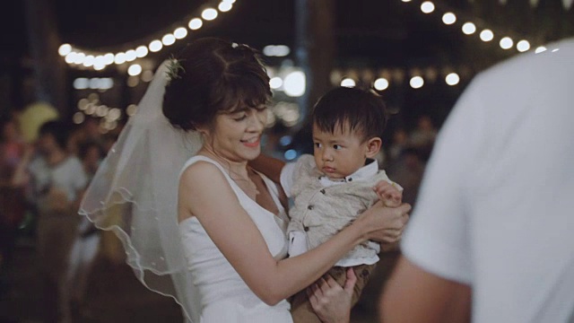 一位亚洲母亲在晚上的婚礼上抱着一个男婴。视频素材