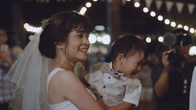 一位亚洲母亲在晚上的婚礼上抱着一个男婴。视频素材