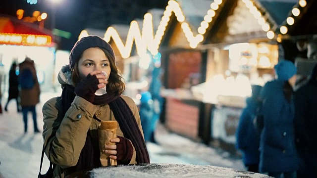 在圣诞市场上吃着面包喝着热饮的女人视频下载