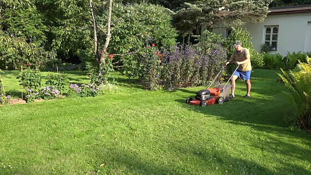男园丁在自家院子里推着割草机。FullHD视频下载