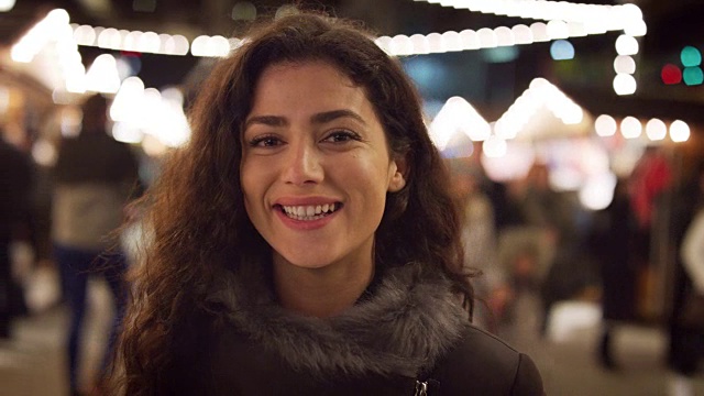 微笑的女人在夜晚享受圣诞市场的肖像视频素材