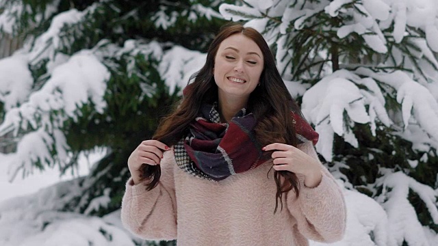 一个快乐的女人的肖像谁是走在她的头发在冬天的森林，女士是摆姿势旁边的一棵雪树视频素材
